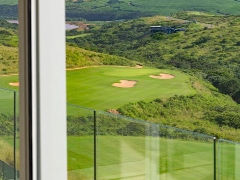 A scenic view overlooking a lush green golf course with sand bunkers, framed by a modern glass balustrade.