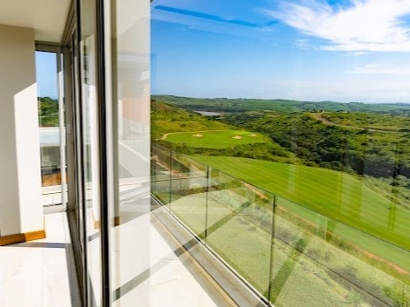 A modern balcony featuring a sleek glass balustrade and tiled flooring, offering expansive views over the surrounding golf course landscape.