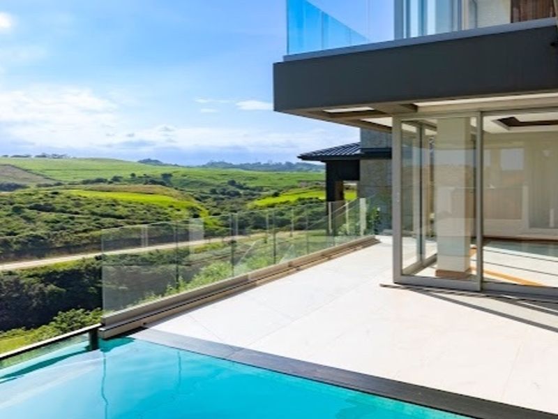 Modern infinity edge swimming pool with glass balustrade and expansive views, featuring seamless indoor-outdoor flow through large sliding glass doors.