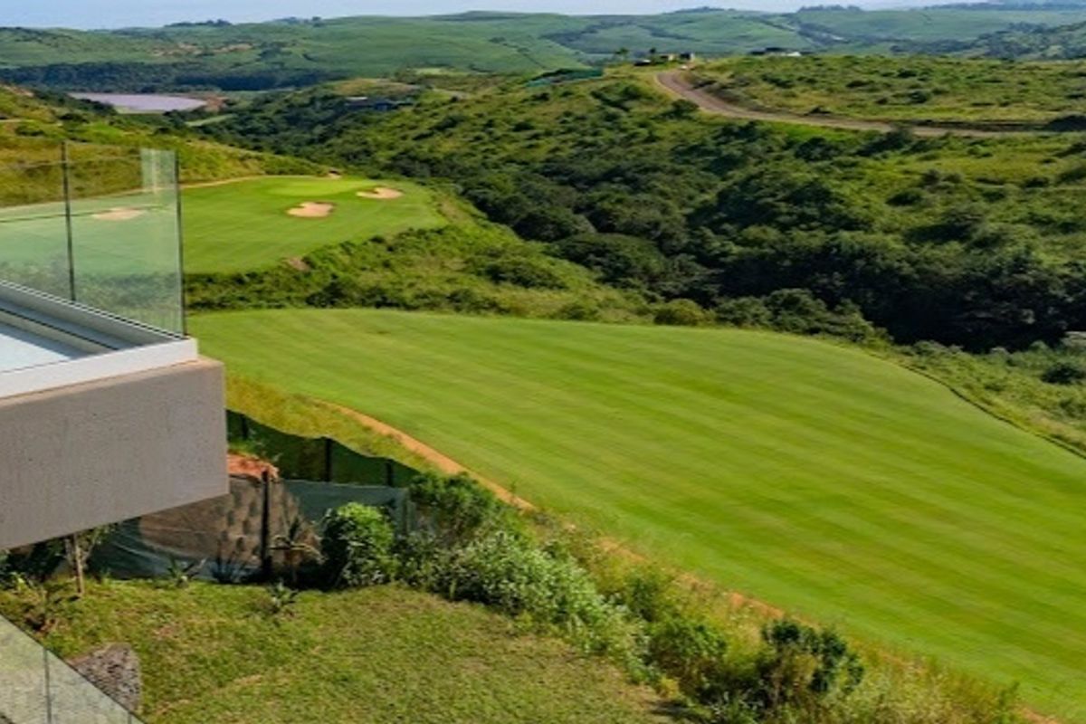 Elevated view overlooking a lush green golf course and rolling hills, featuring a modern glass balustrade in the foreground.