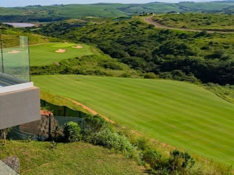 Elevated view overlooking a lush green golf course and rolling hills, featuring a modern glass balustrade in the foreground.