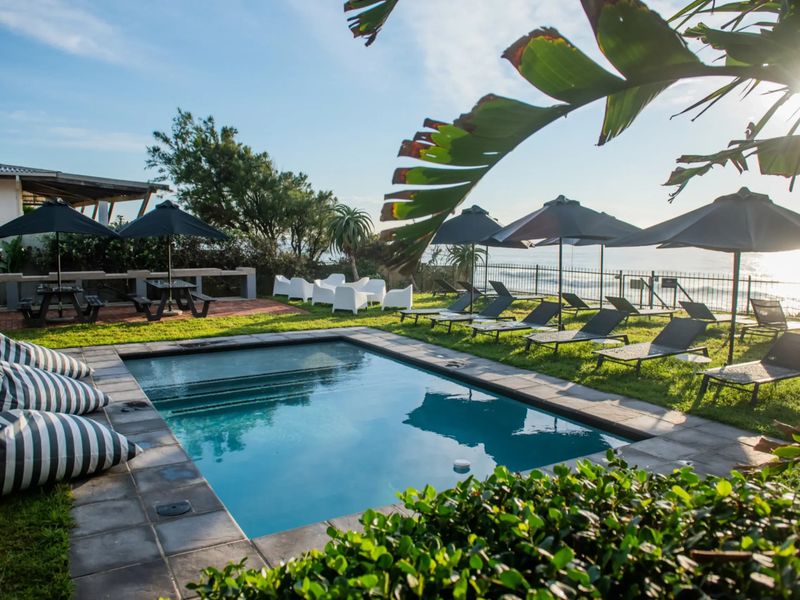 A well-maintained outdoor swimming pool area featuring stone coping, lush lawn, and secure perimeter fencing with ocean views.