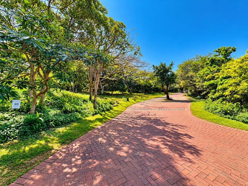 A well-maintained residential plot featuring a paved driveway, mature trees, and established garden landscaping in a serene setting.
