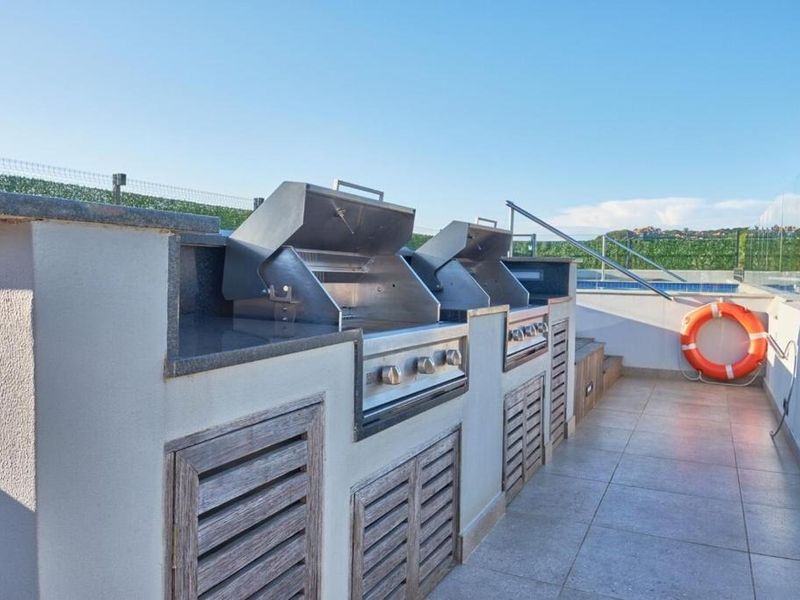 Outdoor pool area featuring a modern built-in barbecue station with granite countertops, tiled flooring, and a glass balustrade overlooking the swimming pool.