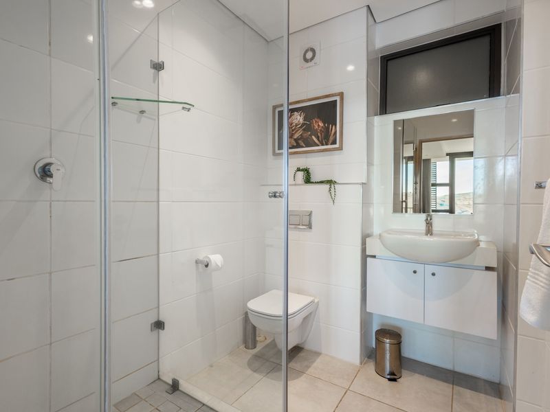 Modern bathroom featuring a glass-enclosed shower, wall-mounted toilet, and a sleek vanity basin with integrated storage.