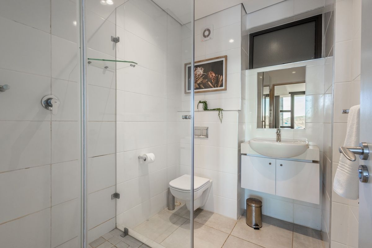 Modern bathroom featuring a glass-enclosed shower, wall-mounted toilet, and a sleek vanity basin with integrated storage.
