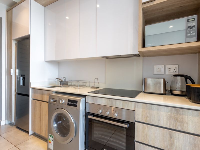 Modern kitchen featuring sleek white and wood-grain cabinetry, stone countertops, integrated appliances, and a built-in oven with electric hob.
