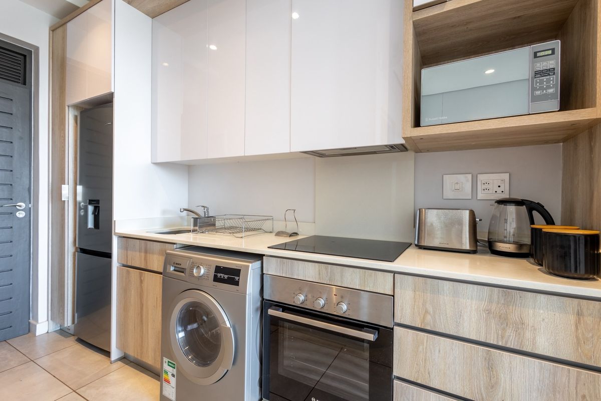Modern kitchen featuring sleek white and wood-grain cabinetry, stone countertops, integrated appliances, and a built-in oven with electric hob.