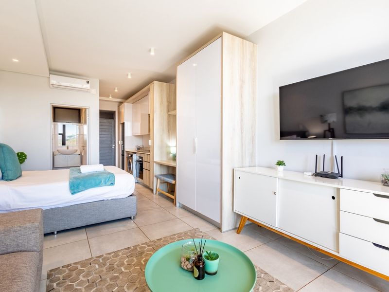 Modern open-plan studio apartment featuring tiled floors, built-in cabinetry, a compact kitchenette, and an en-suite bathroom with air conditioning.