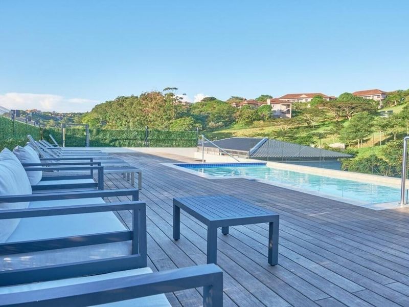 A well-maintained outdoor pool area featuring timber decking, a glass balustrade, and scenic views of the surrounding landscape.