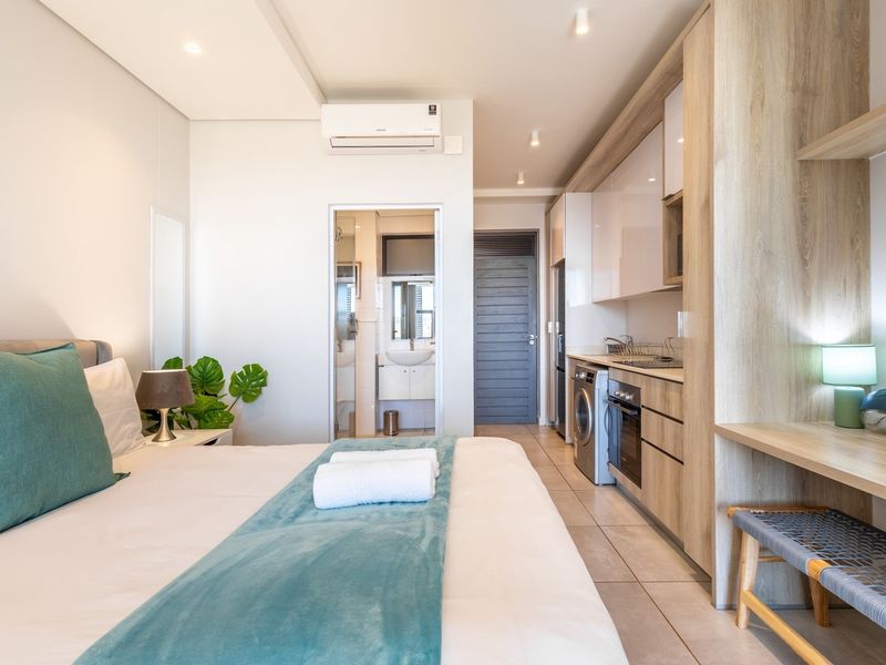 Modern open-plan studio apartment featuring a compact kitchenette with built-in appliances, tiled flooring, air conditioning, and an en-suite bathroom.