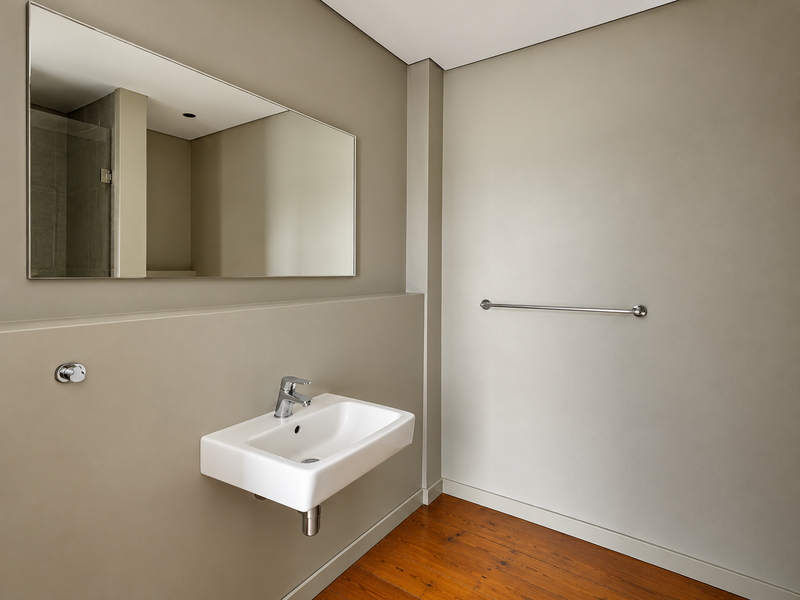 A modern, minimalist bathroom featuring a wall-mounted basin, chrome fixtures, a large mirror, and warm timber flooring.