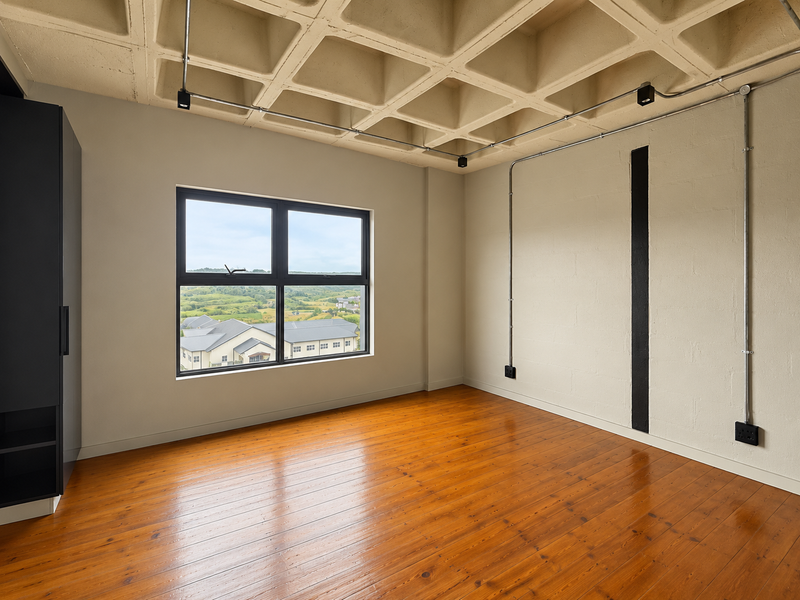 A bright, empty bedroom featuring polished hardwood floors, a unique waffle slab ceiling, exposed conduit lighting, and a built-in wardrobe with scenic window views.