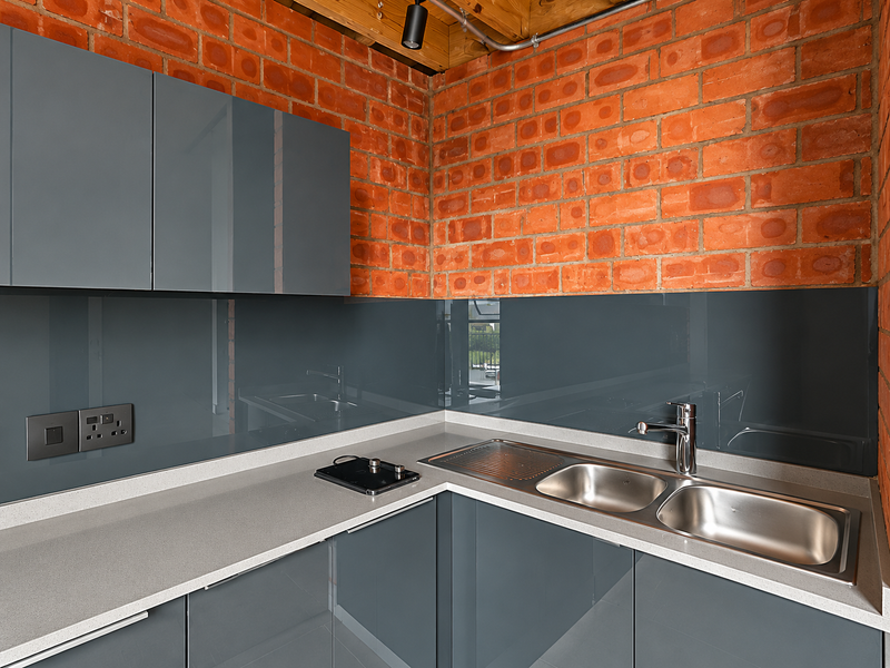 Modern kitchen area featuring sleek grey cabinetry, stone countertops, a stainless steel double sink, and a striking exposed brick wall with timber ceiling beams.