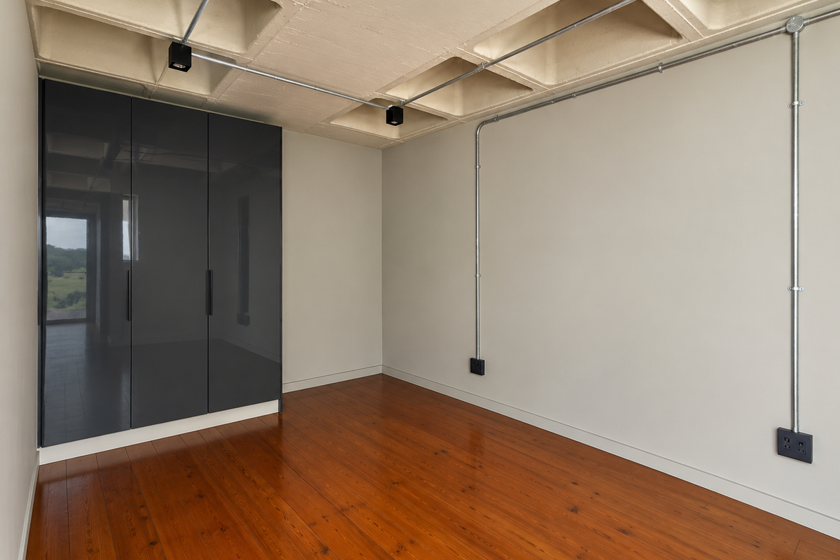 Modern bedroom featuring polished hardwood floors, built-in dark grey cabinetry, and an industrial-style exposed concrete waffle ceiling with surface-mounted electrical conduits.
