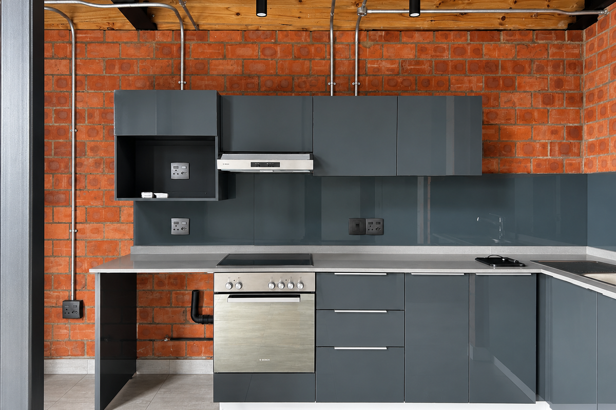Modern industrial-style kitchen featuring grey cabinetry, stone countertops, built-in oven, electric hob, and exposed brick walls with timber ceiling beams.