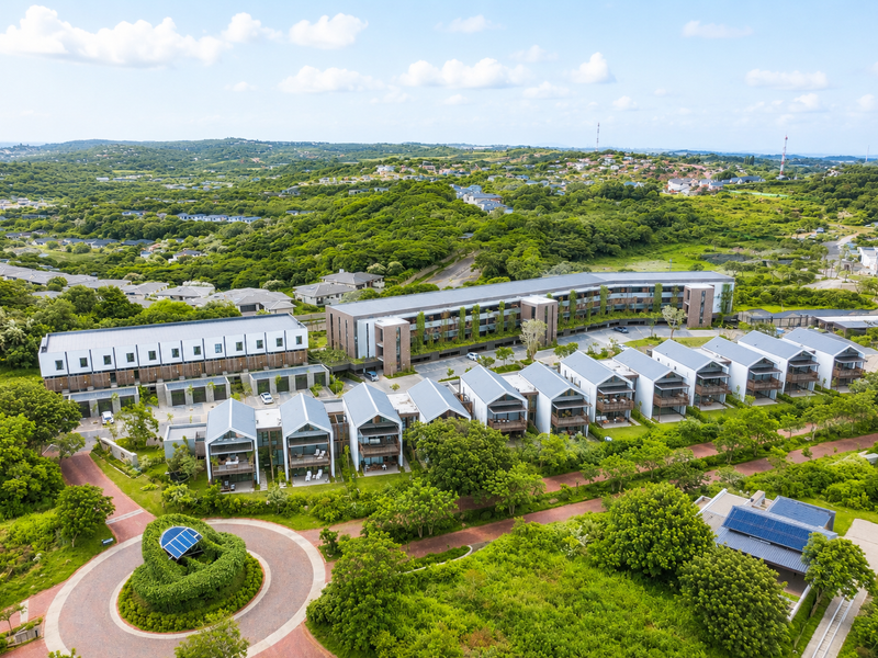 Aerial view of a modern residential apartment complex featuring multiple units, landscaped grounds, and paved access roads in a lush green setting.