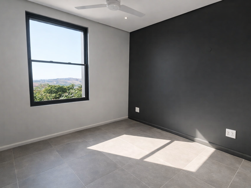 A modern, empty bedroom featuring neutral grey tiled flooring, a striking black accent wall, and a ceiling fan with views through a large window.