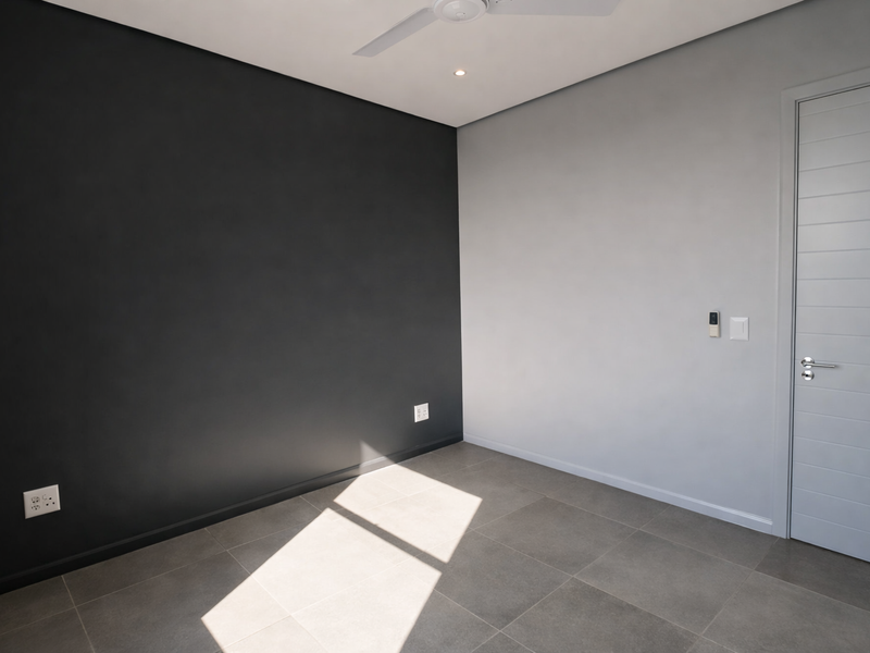A modern, empty bedroom featuring neutral grey and charcoal walls, large format floor tiles, a ceiling fan, and recessed lighting.