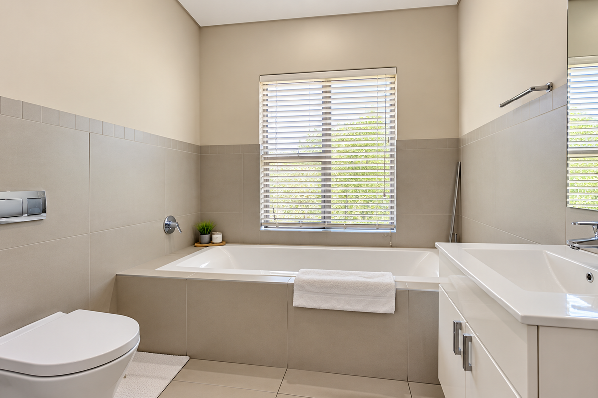 Modern bathroom featuring a built-in bathtub, wall-mounted toilet, and a sleek vanity with basin, complemented by neutral wall tiles and natural light.