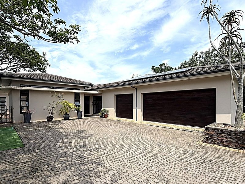 Front elevation of a modern house featuring a paved driveway, double garage, and stone-clad accents under a tiled roof.