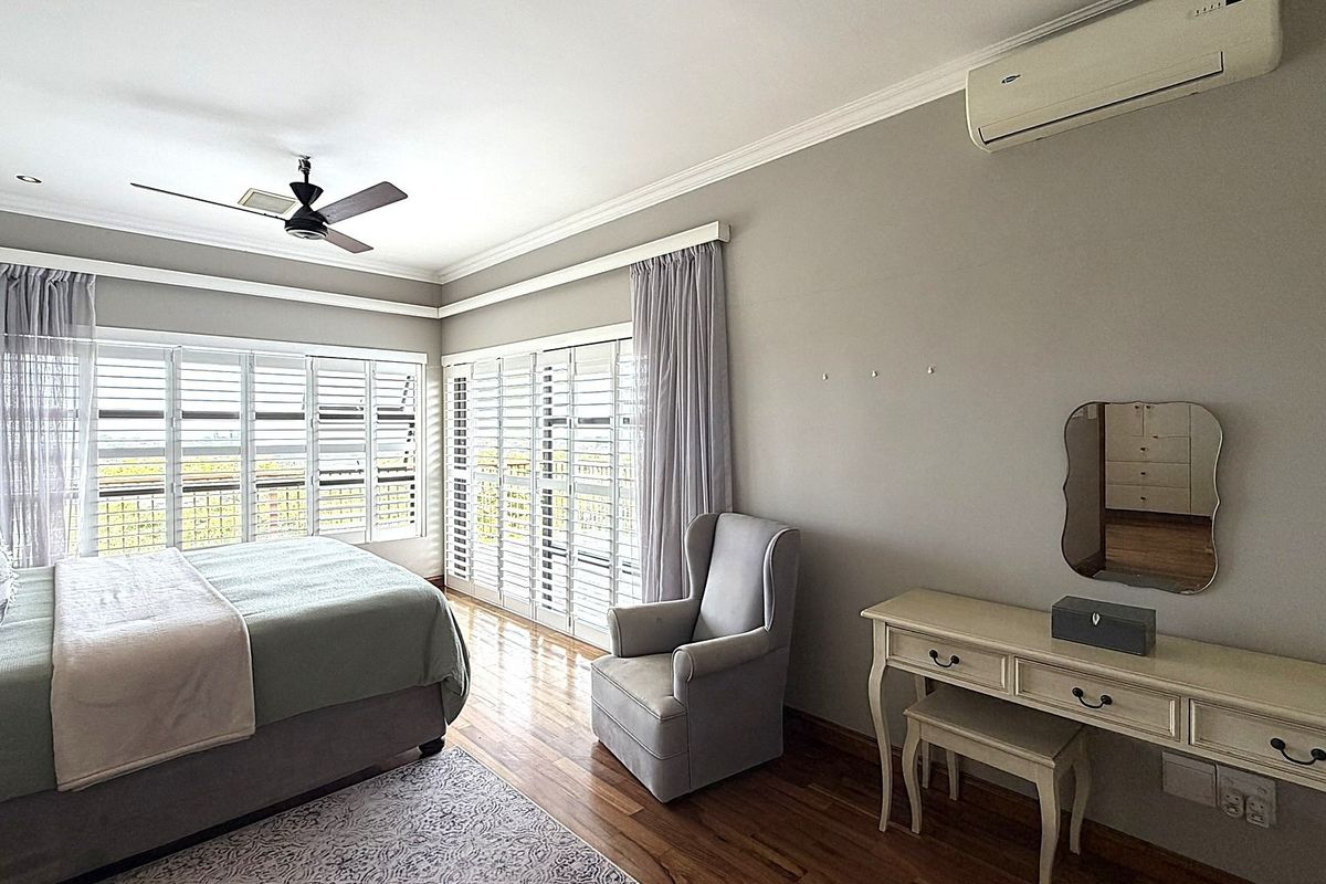 Spacious bedroom featuring hardwood flooring, plantation shutters, crown molding, a ceiling fan, and a wall-mounted split-system air conditioner.