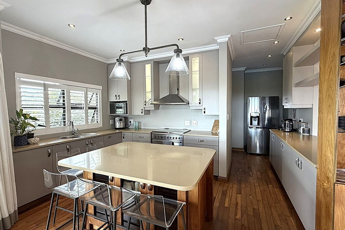 Modern kitchen featuring a central island with stone countertops, stainless steel appliances, timber flooring, and elegant recessed lighting throughout the space.
