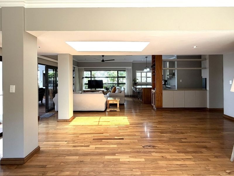 Spacious open-plan living area featuring warm hardwood flooring, a large central skylight, and seamless flow to the outdoor patio through sliding glass doors.
