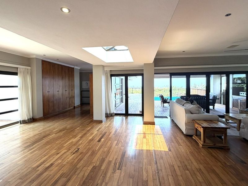 Spacious open-plan living area featuring rich hardwood flooring, a central skylight, recessed lighting, and seamless access to the outdoor patio through sliding glass doors.
