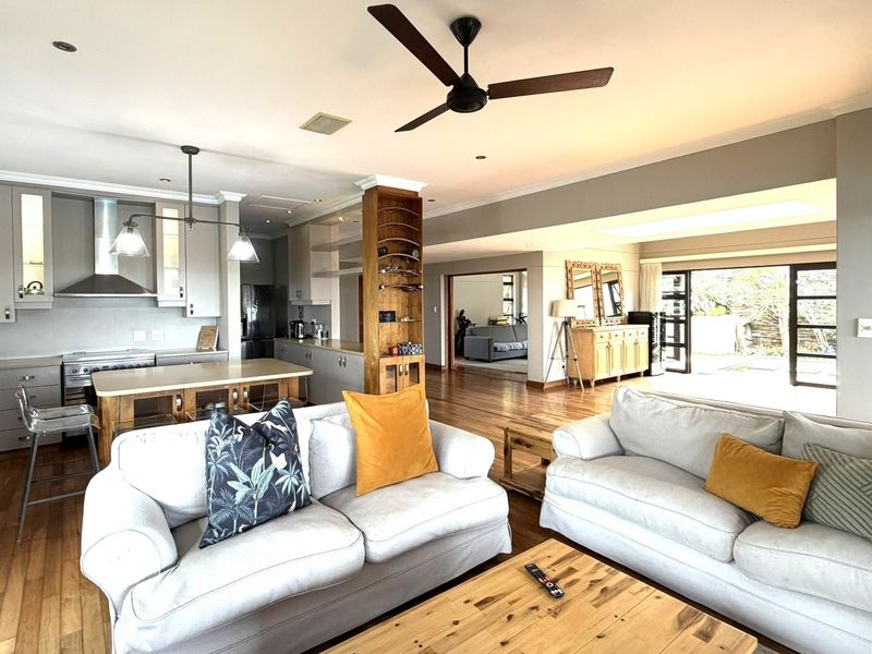 Spacious open-plan living area featuring hardwood floors, a modern kitchen with a central island, and seamless flow to the outdoor patio through sliding doors.