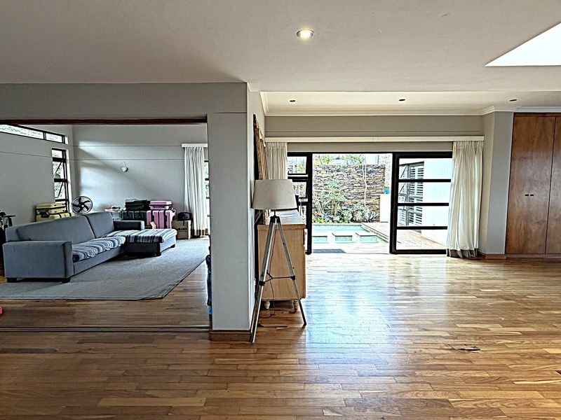 Spacious open-plan living area featuring polished hardwood flooring, a large skylight, and seamless indoor-outdoor flow through stacking doors to the pool area.