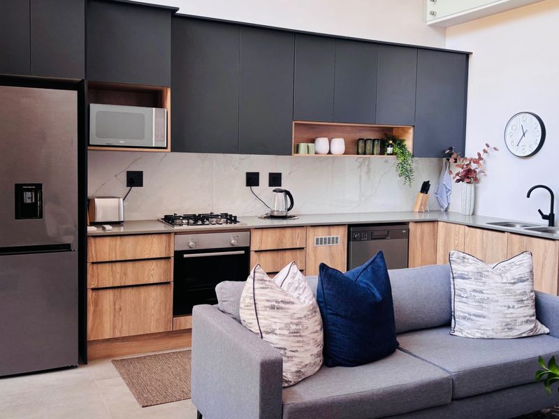 Modern open-plan kitchen featuring sleek matte black and wood-grain cabinetry, stone countertops, marble-look splashback, and integrated appliances.