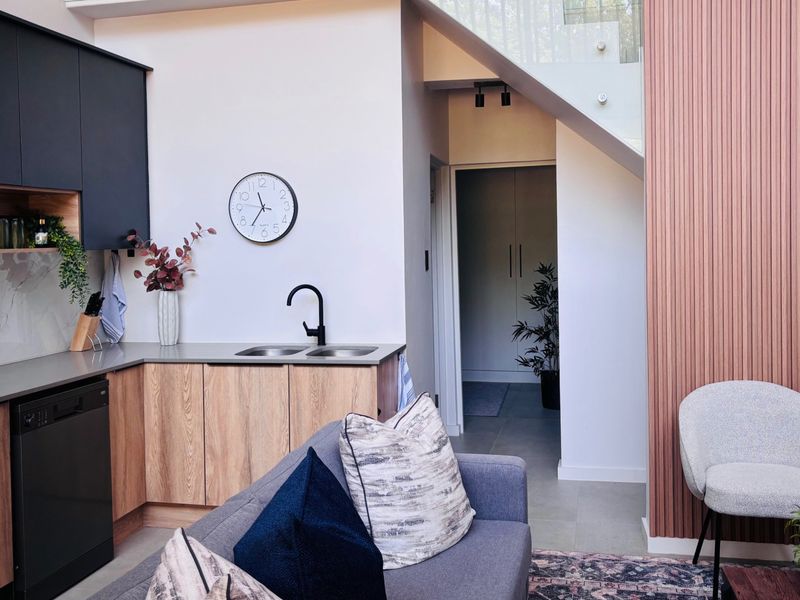 Modern open-plan kitchen area featuring sleek cabinetry, integrated appliances, and a contemporary staircase with glass balustrade and decorative timber wall paneling.