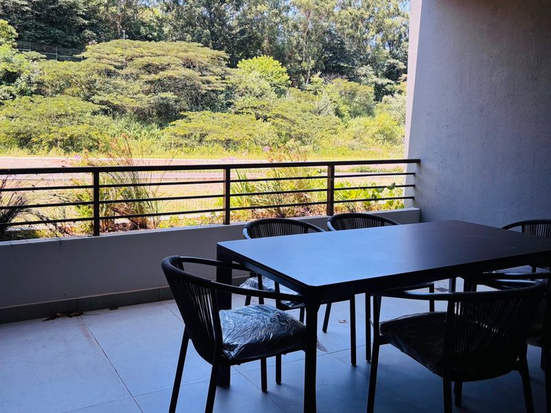 A covered balcony featuring tiled flooring and a metal balustrade, offering a pleasant outlook over the surrounding greenery.