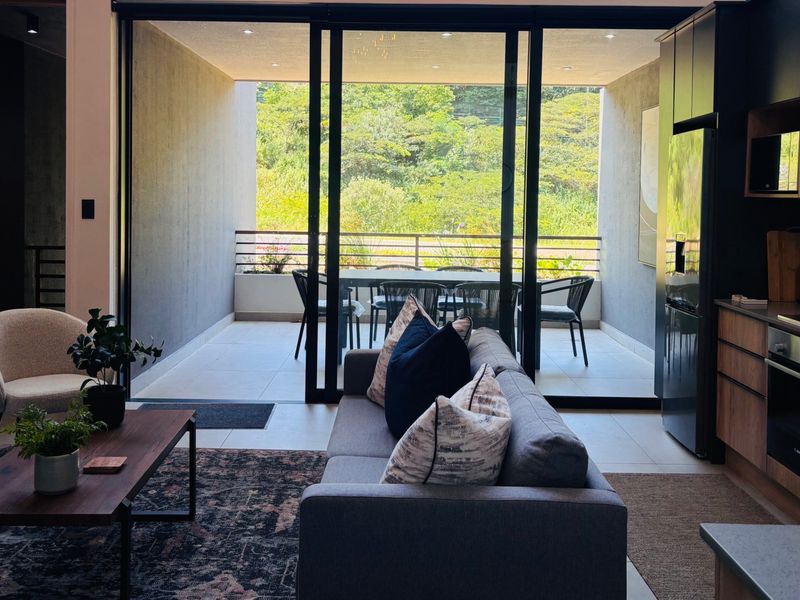 Modern open-plan living area featuring a sleek kitchen with integrated appliances and seamless flow to a covered balcony with scenic views.