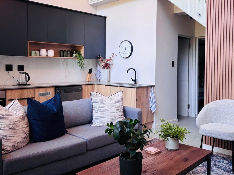 Modern open-plan living area featuring a sleek kitchen with dark cabinetry, stone countertops, integrated appliances, and stylish timber-look wall panelling.