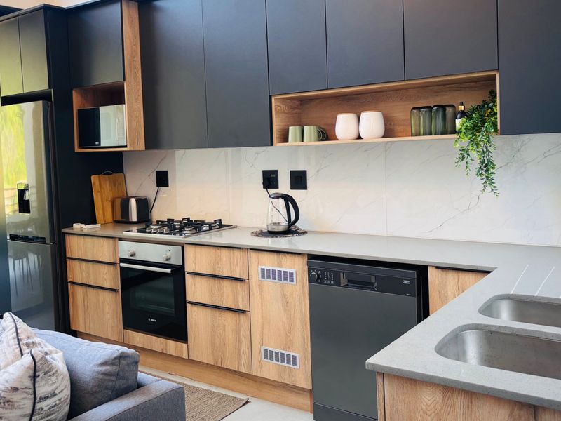 Modern open-plan kitchen featuring sleek dark and wood-tone cabinetry, stone countertops, integrated appliances, and a stylish marble-look splashback.