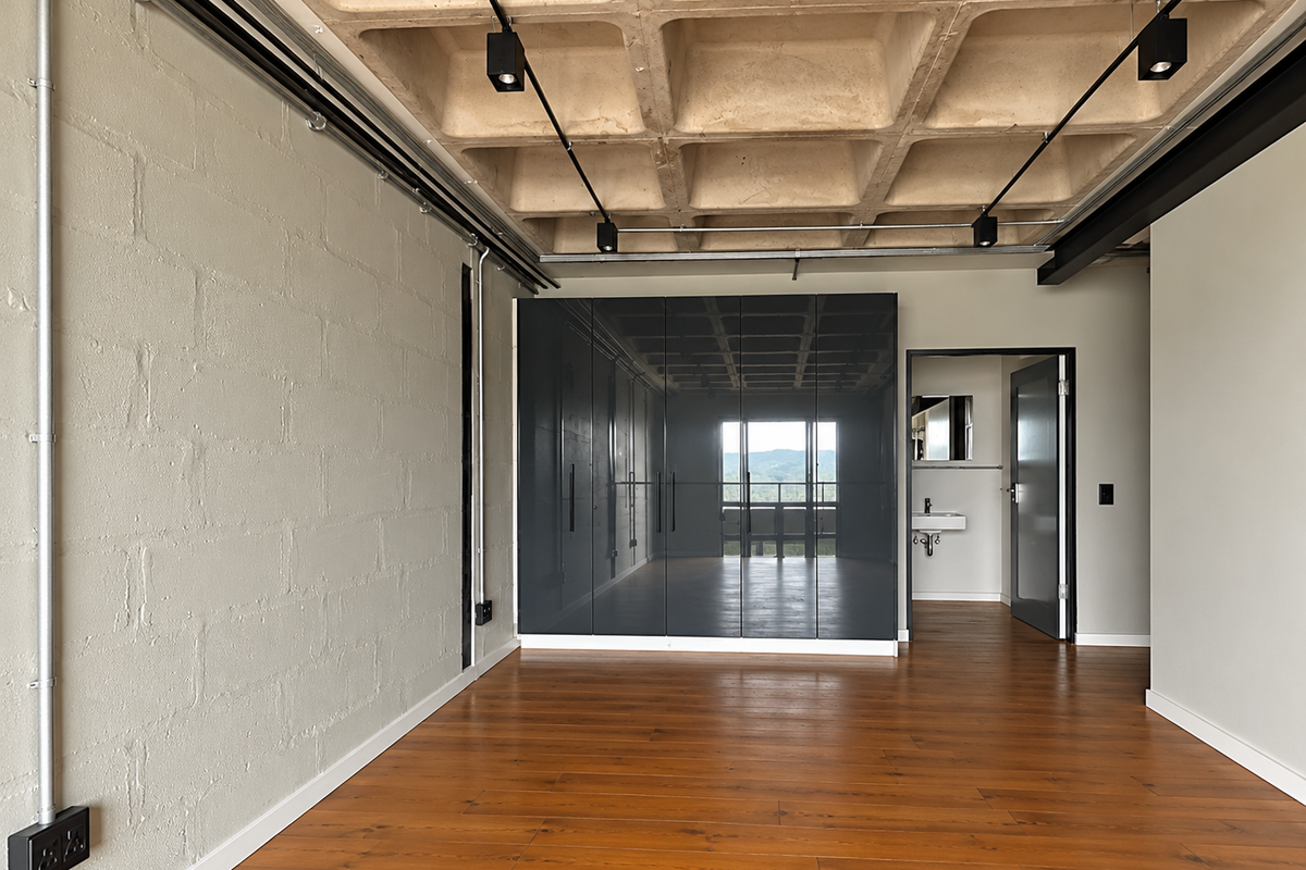 Modern bedroom featuring an exposed concrete waffle ceiling, built-in high-gloss wardrobes, and industrial-style exposed electrical conduit, with direct access to an en-suite bathroom.