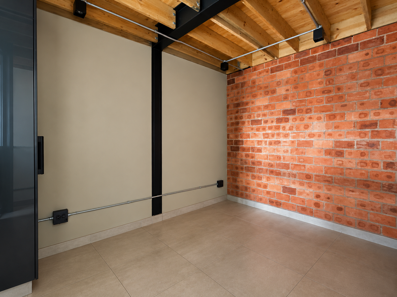Modern industrial-style living space featuring exposed brickwork, timber ceiling beams, and polished tile flooring with exposed electrical conduit detailing.