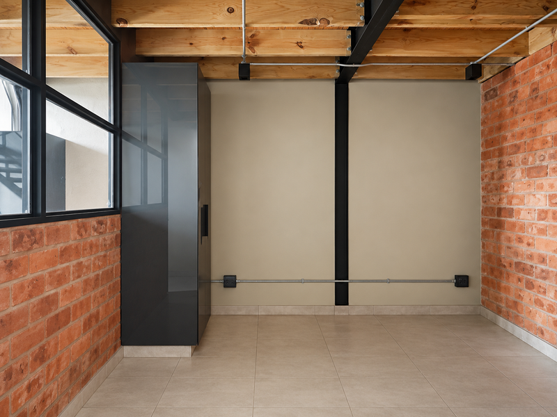 A modern industrial-style room featuring exposed brick walls, timber ceiling beams, tiled flooring, and a sleek built-in cabinet with black metal window frames.