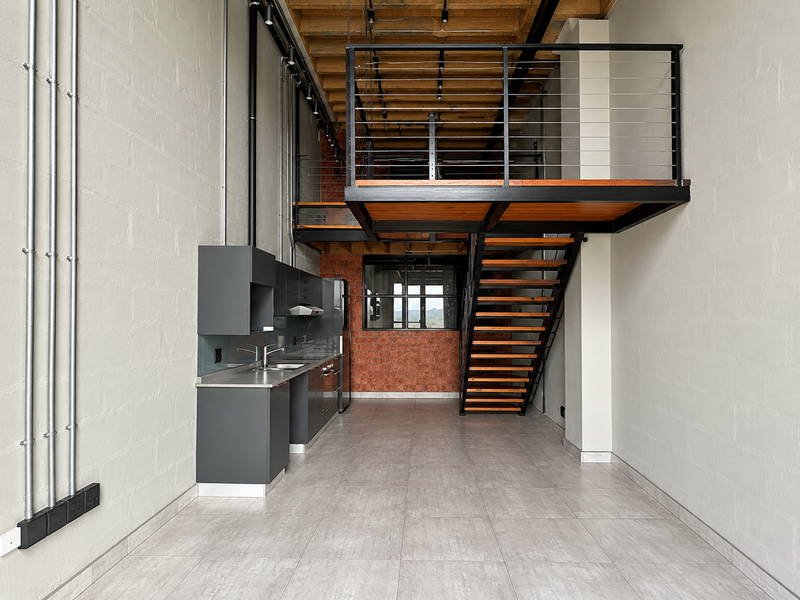 Modern industrial-style open-plan apartment featuring a mezzanine level, exposed brickwork, timber staircase, and a sleek built-in kitchen with contemporary finishes.