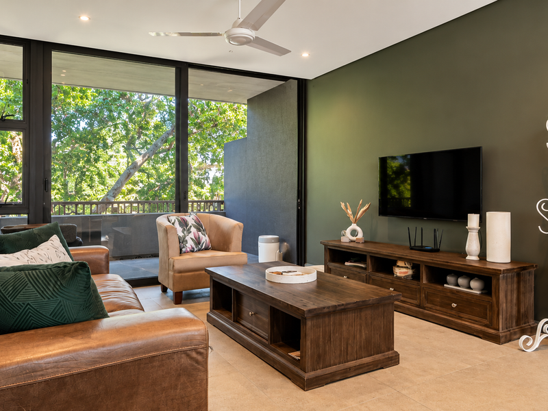 A well-maintained living room featuring large sliding glass doors that open to a balcony, tiled flooring, and modern recessed lighting.