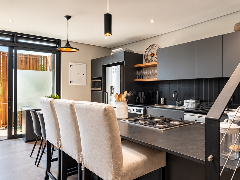 Modern open-plan kitchen featuring sleek dark cabinetry, a gas cooktop, and seamless indoor-outdoor flow to a private balcony through large sliding glass doors.