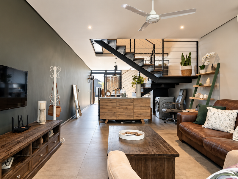 Spacious open-plan living area featuring modern tiled floors, a striking staircase, ceiling fan, and integrated air conditioning.