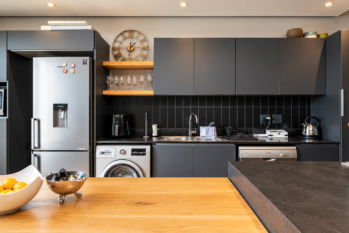 Modern kitchen featuring dark matte cabinetry, subway tile backsplash, integrated appliances, and a wooden breakfast bar with stone countertops.