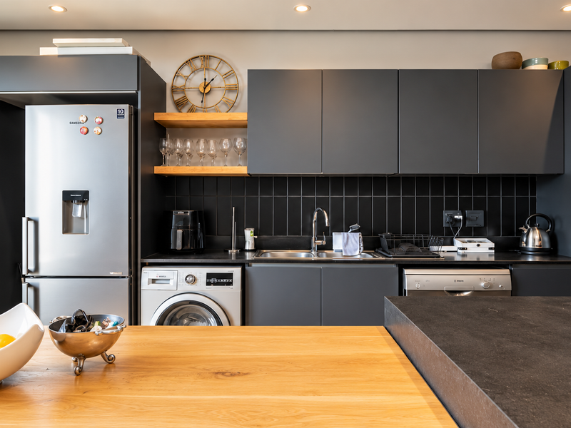 Modern kitchen featuring dark matte cabinetry, subway tile backsplash, integrated appliances, and a wooden breakfast bar with stone countertops.