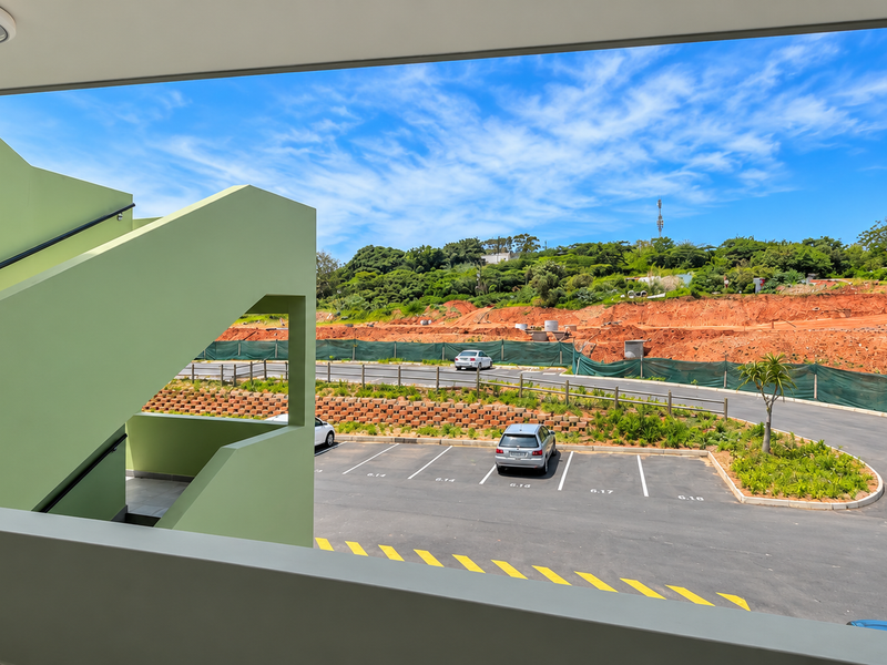 A view from a balcony overlooking a parking area and surrounding landscape with a modern staircase structure visible.
