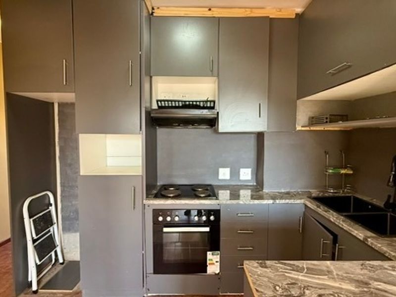 Compact kitchen featuring dark grey cabinetry, stone-look countertops, integrated electric hob and oven, and a modern black sink fixture.