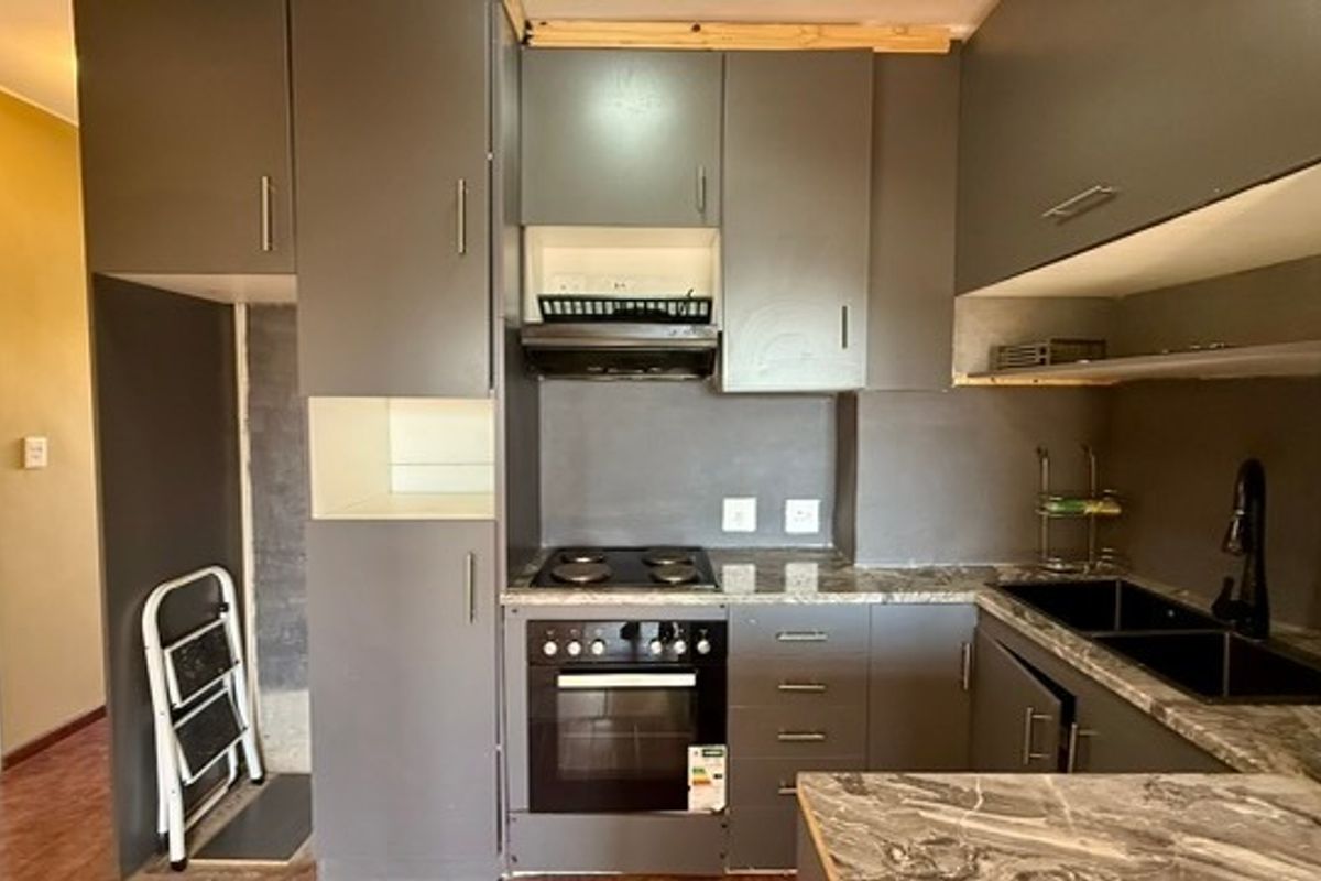 Compact kitchen featuring dark grey cabinetry, stone-look countertops, integrated electric hob and oven, and a modern black sink fixture.