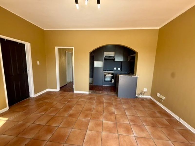 An open-plan living area featuring tiled flooring and an arched transition to a compact kitchen equipped with built-in oven and hob.
